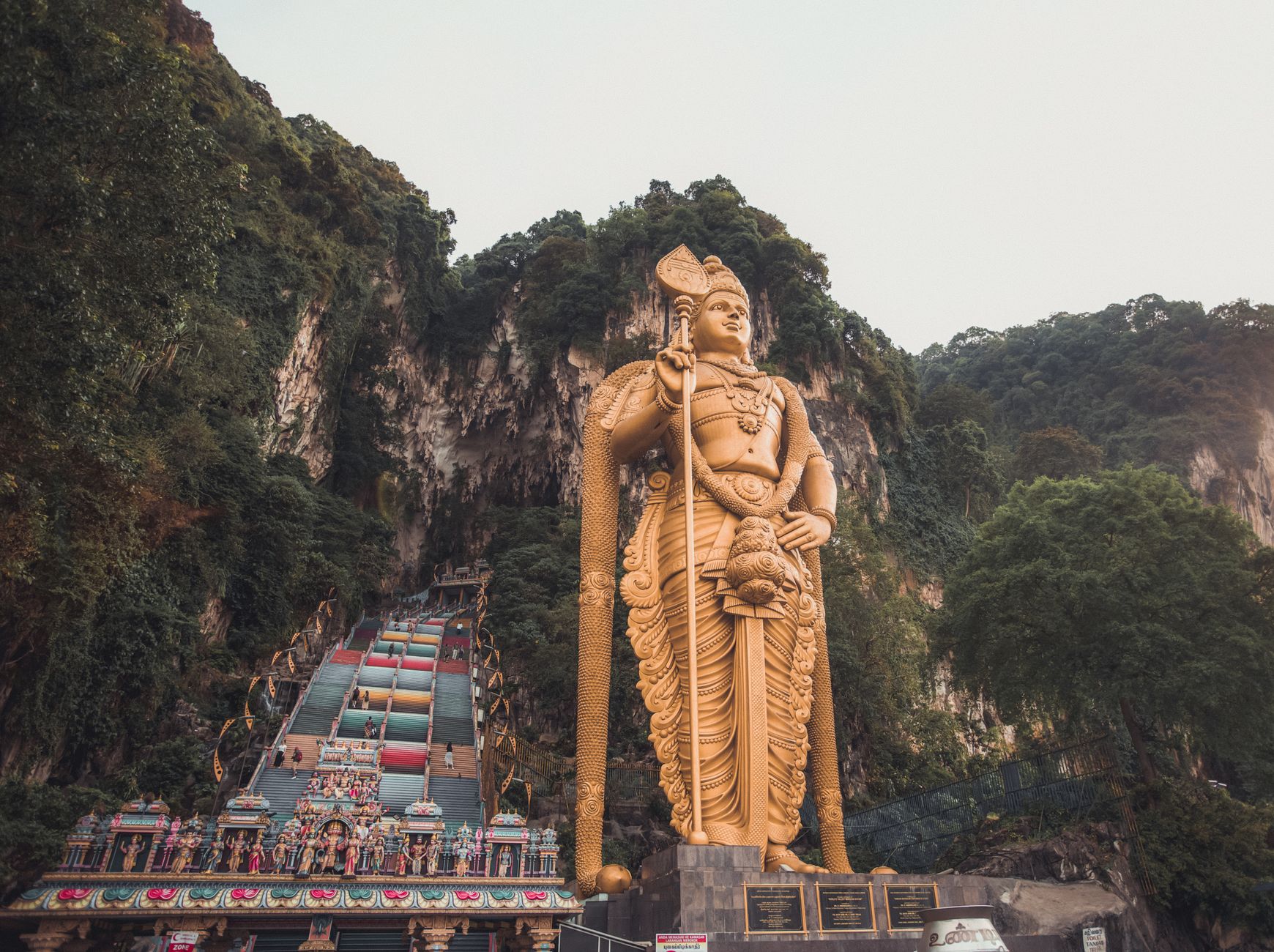 Stunning view of the golden Murugan statue at Batu Caves, Malaysia, surrounded by lush greenery.
