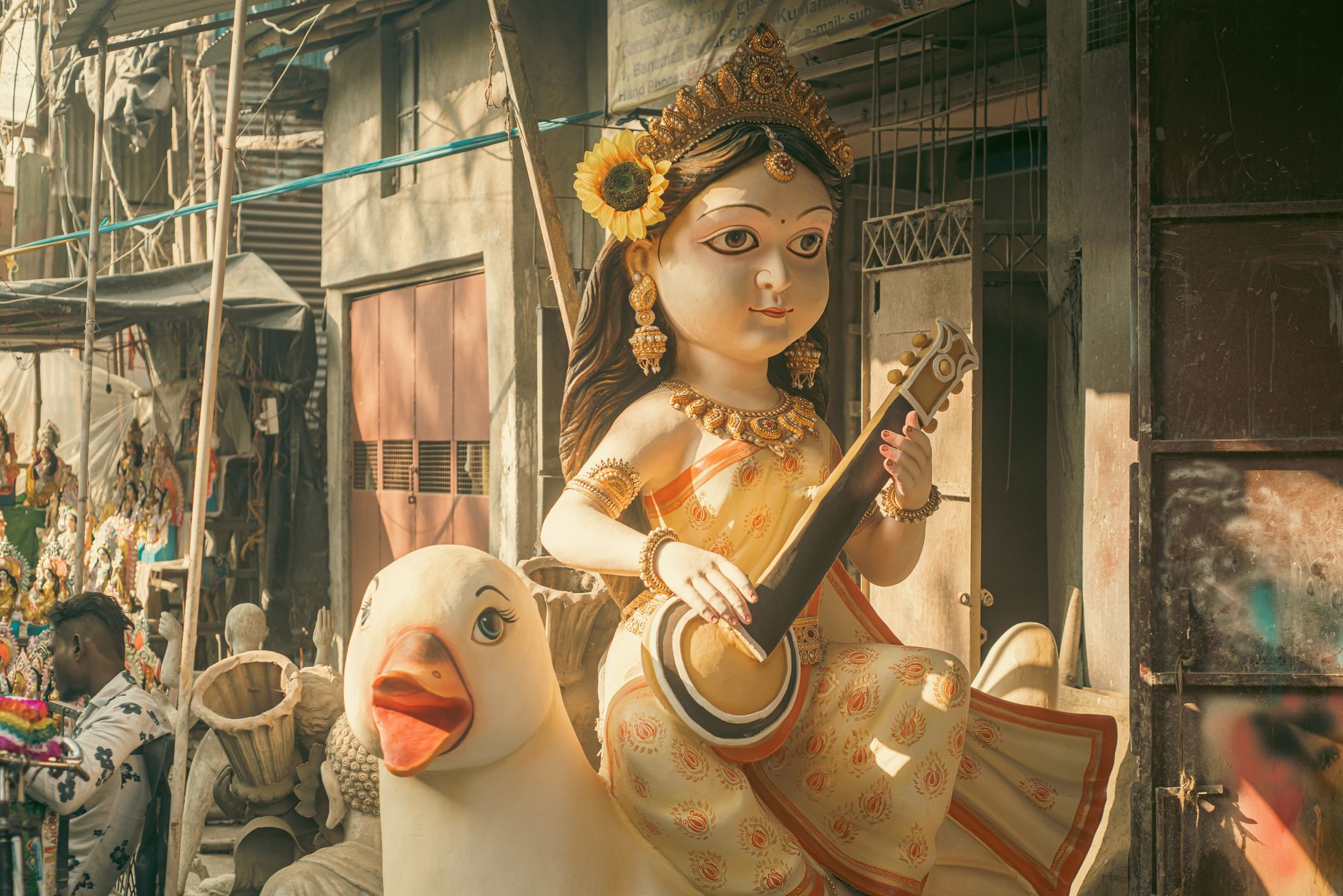 Vibrant Saraswati statue holding veena in outdoor Indian workshop setting, rich cultural crafts.
