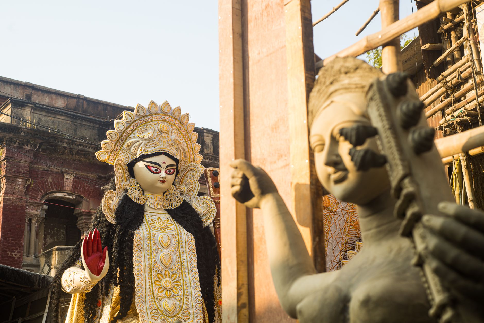Close-up of a vibrant Hindu goddess statue next to an unfinished sculpture in an outdoor setting.