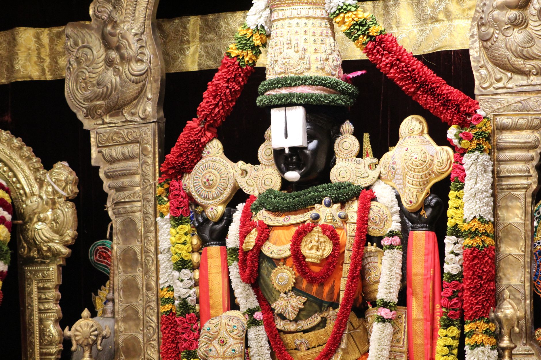 Intricately decorated statue of a Hindu deity adorned with colorful garlands and ornate jewelry.