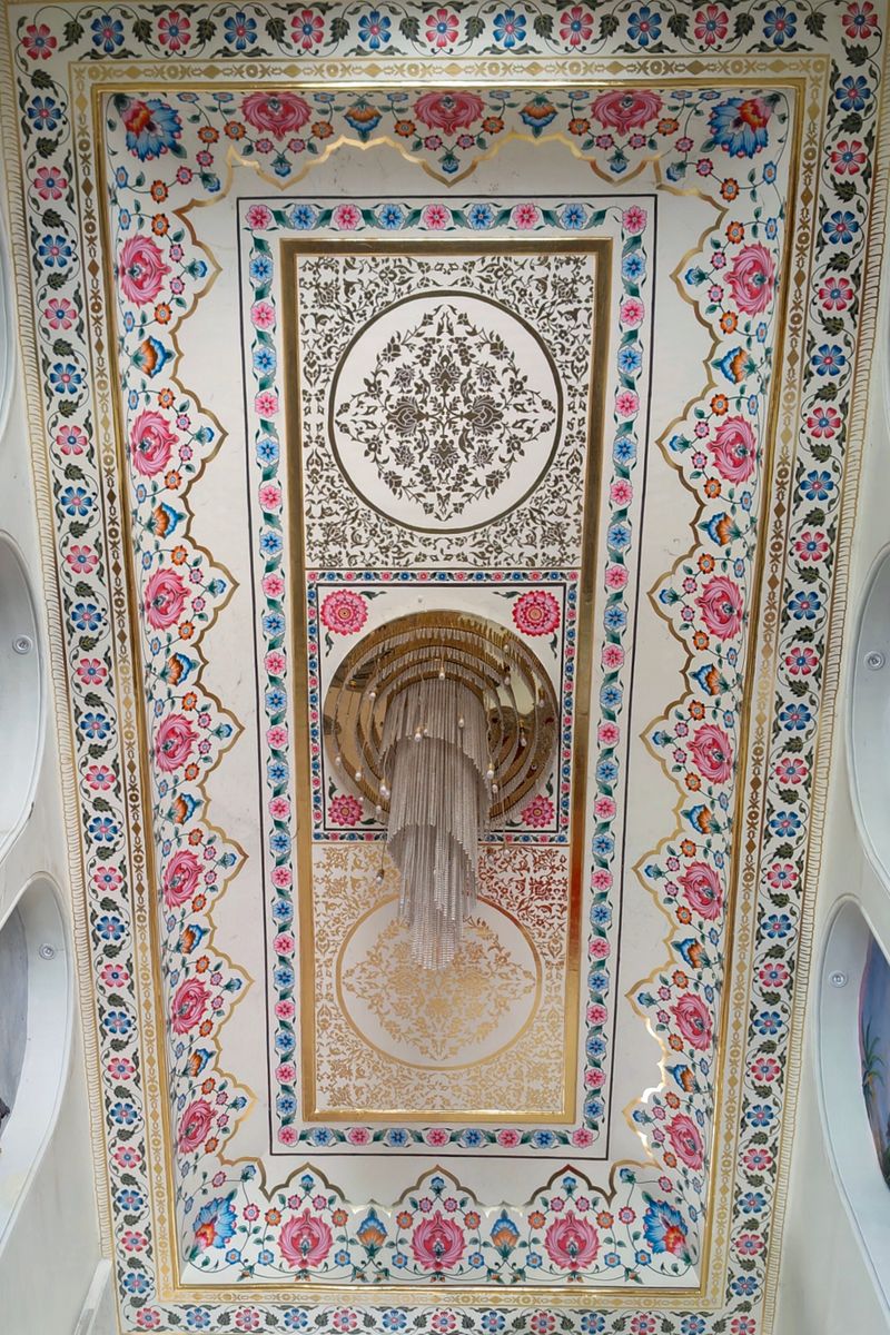 Intricate painted ceiling with floral patterns and chandelier in ISKCON Temple, Panvel, India.