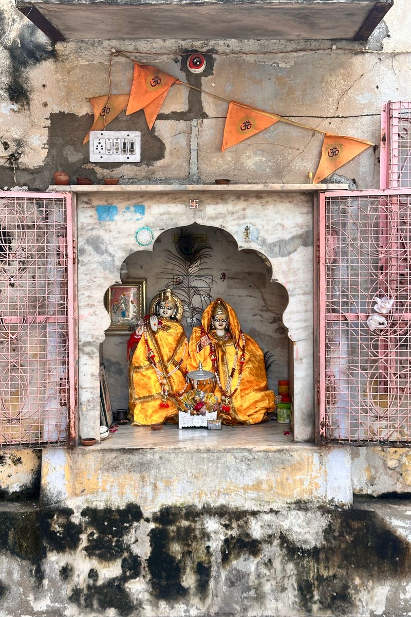 Ornate Hindu shrine with vibrant idols and flags on rustic wall.