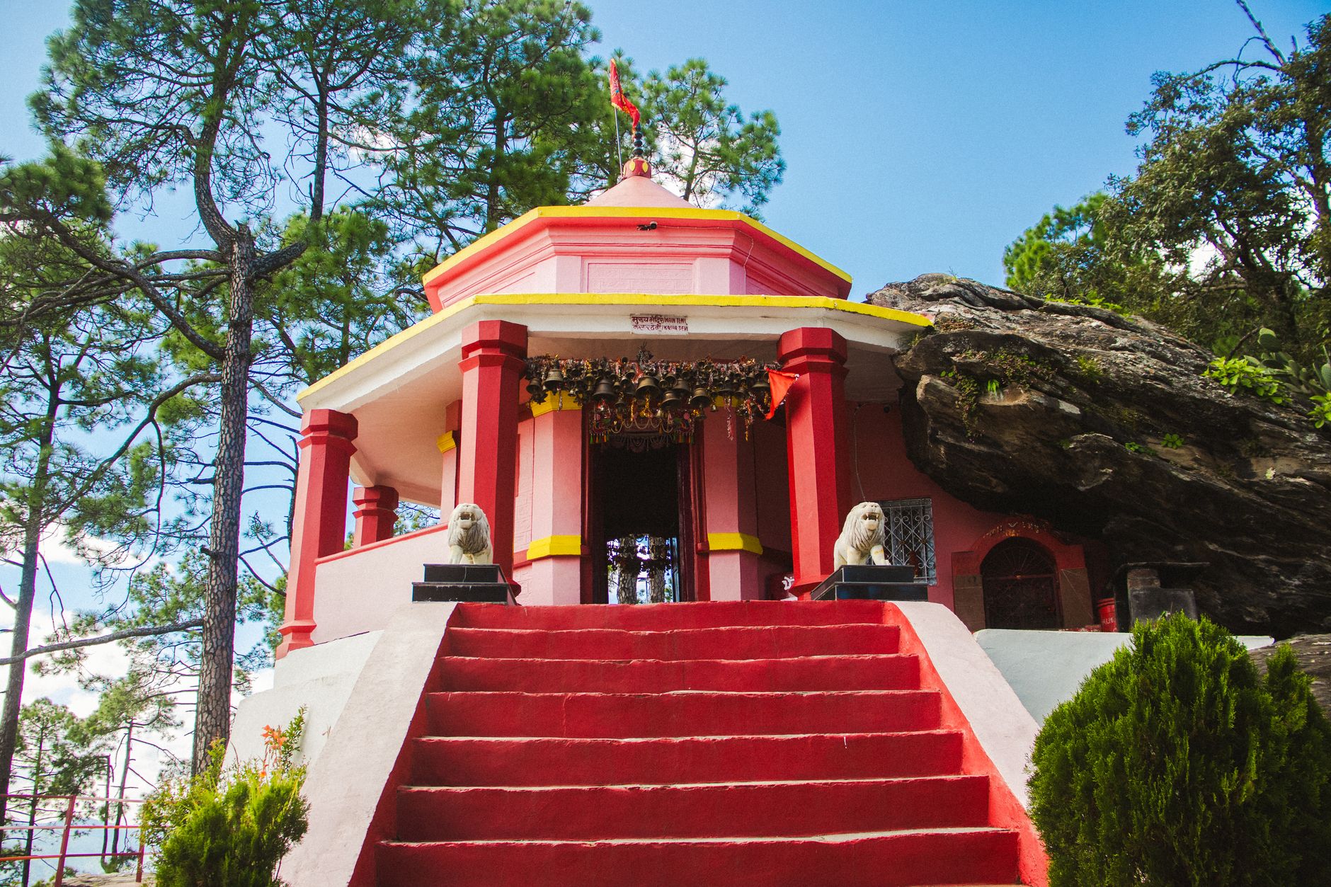 A beautiful Hindu temple surrounded by pine trees in Binsar, Uttarakhand, India, under a clear blue sky.